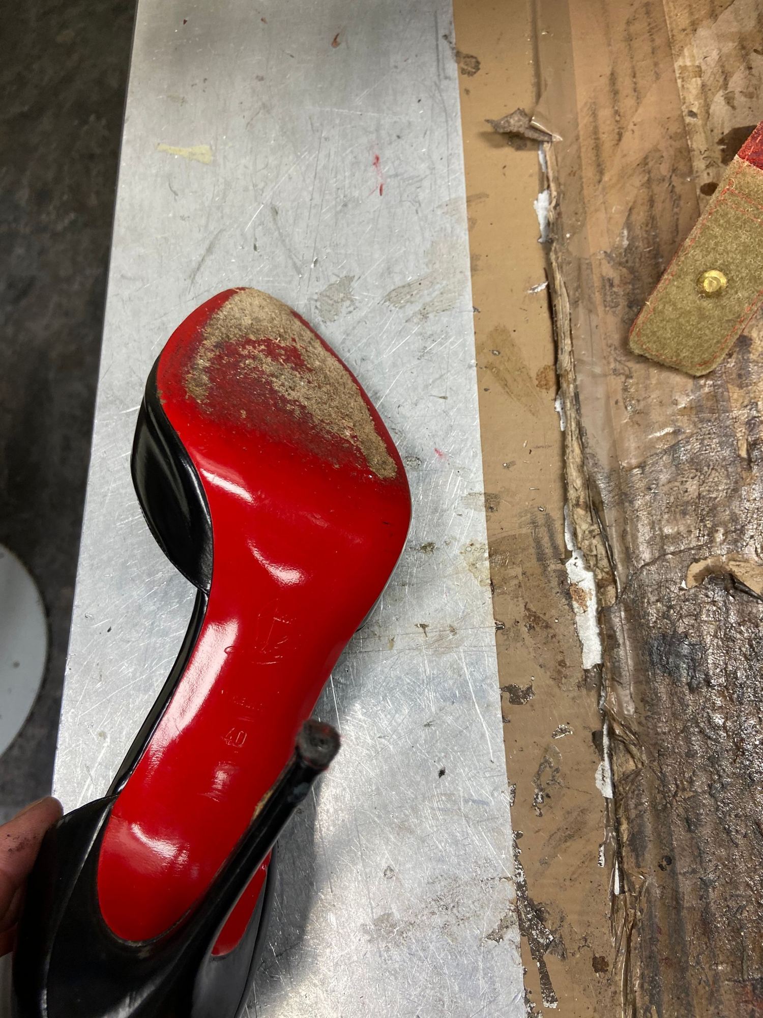 Semelle rouge usée d'un escarpin noir sur plan de travail métallique